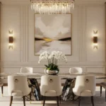 Modern dining room wall decor ideas featuring a large square abstract artwork in neutral tones. The wall includes classic rectangular molding and symmetrical gold lighting, creating an expensive and sophisticated look.